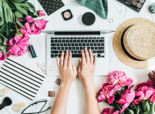 where you can find blogging opportunities. picture is of a ladies hands typing on a laptop, pink bouquets, a straw hat and some makeup